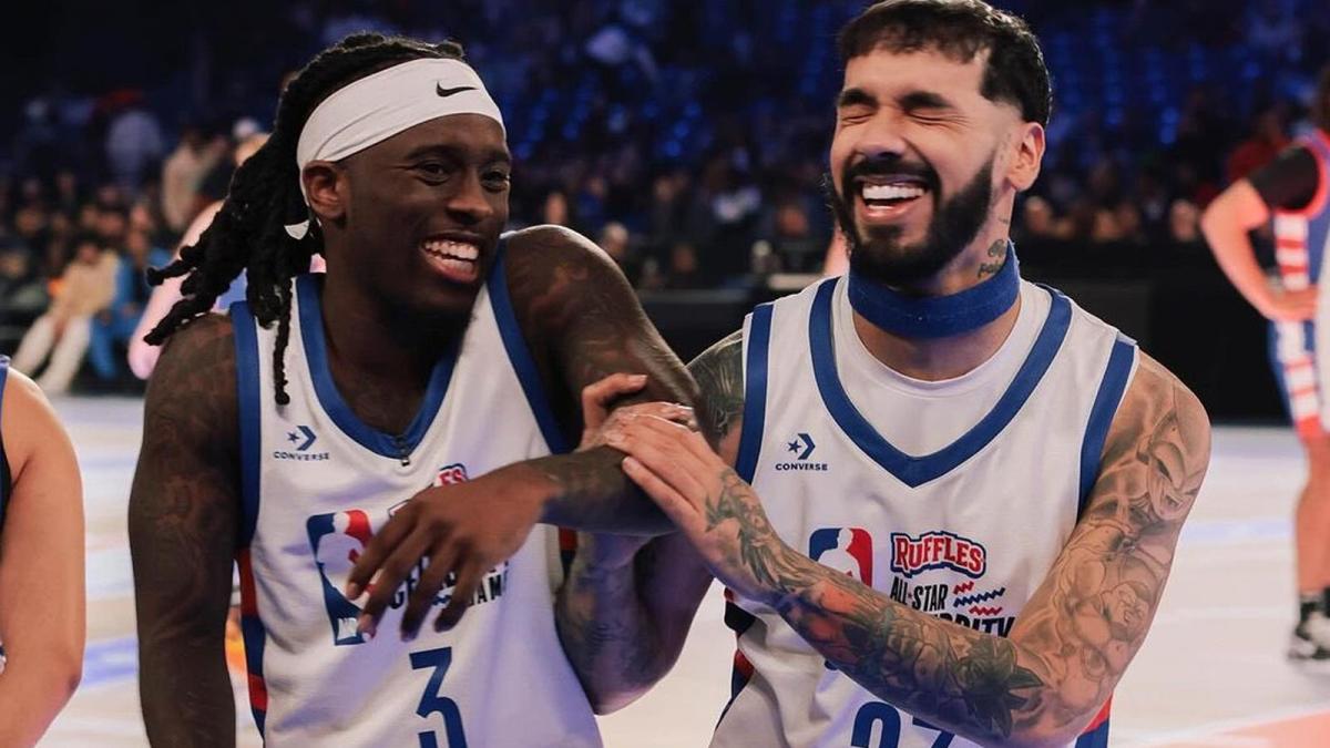 Kai Cenat and Anuel, both of whom are wearing NBA branded basketball playing gear, laugh together courtside during the 2024 Celebrity All-Star Game